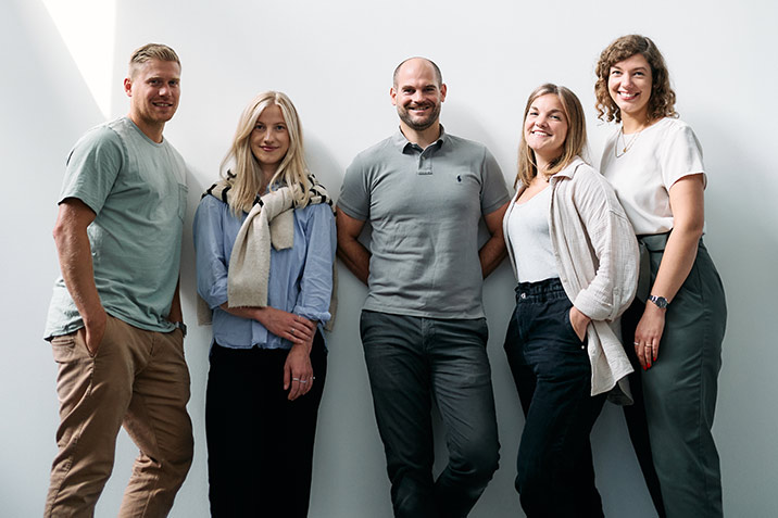 Fünf Kollegen lächeln in die Kamera.